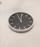 Front view of black-face wall clock showing markers and hands