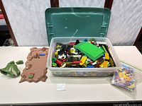 Overall lot showing tub of bricks, terrain baseplate, dinosaur head, manuals bag