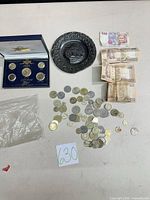 Group shot of entire lot: gold-plated coin set, decorative plate, loose coins, banknotes, plastic bag of additional coins