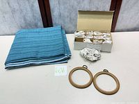 Folded striped textile, boxed glass hummingbirds, two embroidery hoops on tabletop