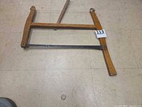 Full view of bucksaw laid flat showing wooden frame and tensioning cord