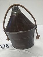 Front view of metal miner’s canteen showing rope handle and cap