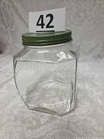 Front view of clear faceted glass jar with green metal lid showing Art Deco rib and leaf motif