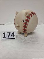 Front angled view of pig-shaped baseball bank showing facial features and seam detail