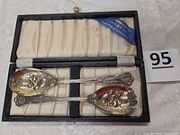 Open presentation case showing both silver-plated berry spoons