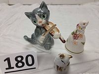 Front view of three porcelain pieces: grey violin cat, rabbit bell, small cat