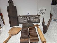 Group shot of all primitive wood items including sign, slaw cutter, rolling pin, cigar mold halves, grater, rug beater, dough paddle