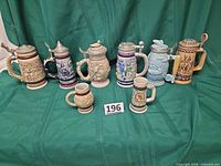 All eight ceramic steins arranged on green cloth showing size comparison