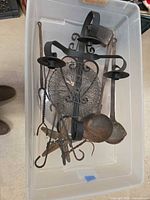 Assortment inside clear bin showing candle sconce, ladles, mesh trivet and other metal pieces