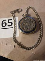 Closed pocket watch with attached chain showing timberwolf relief on lid