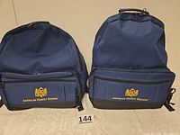 Front view of both navy blue American Orient Express backpacks showing logo and front pockets
