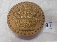 front of round faux wood plaque showing basket and floral relief with dotted border