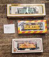 Three boxed Bachmann HO scale cabooses in packaging: green BN, yellow, orange UP
