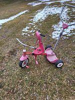 Side view of pink Radio Flyer tricycle showing push handle and overall wear