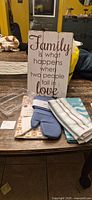 All items on table showing sign, dish mat in package, three tea towels, oven mitt