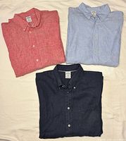 Three folded shirts in red, light blue and navy showing collars and chest pocket areas