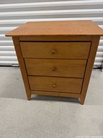 Front view of three-drawer wooden nightstand wood finish