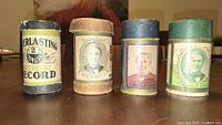 Front view of four wax cylinder tubes showing branding and Edison portraits