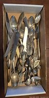 Box holding mixed cutlery showing variety of spoons, forks, knives, novelty pieces