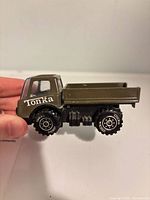 Left side view of Tonka army green dump truck showing logo, wheels, cargo bed