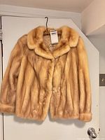 Front view of waist-length honey mink fur coat on hanger