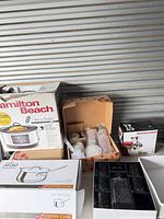 Overview showing boxed Hamilton Beach slow cooker, All-Clad saucepan, KitchenAid attachment, crystal set, wrapped accessories