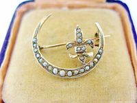 Front view of brooch showing crescent, fleur-de-lis, and seed pearls inside velvet box