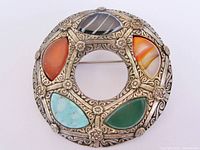front view of circular brooch showing six coloured glass cabochons and detailed metalwork