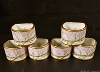 Front view of six matching napkin rings showing painted landscape and gilt rims