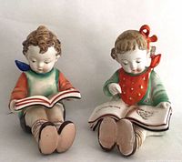 Front view of both figurines seated with books