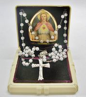 Rosary draped over open cream celluloid box showing Sacred Heart image and velvet lining