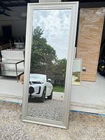 Full view of vertical silver-framed floor mirror standing outdoors
