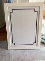 Front view of rectangular fabric bulletin board with purple trim inside white wood frame