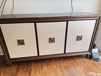 Front view of brown wood frame sideboard with three cream textured doors and metal pulls