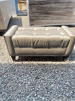 Front view of tufted taupe faux leather bench on gravel