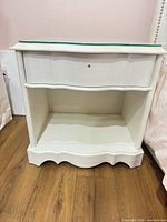 front view of white French Provincial nightstand showing drawer, open shelf, scalloped base