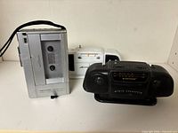 Group shot of silver cassette recorder, black SunTone radio and white radio body