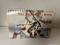 Front cover of spiral-bound book showing title “The Techniques Book” and brush painting imagery