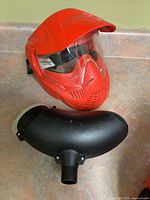 Red full-face paintball mask with clear visor beside black hopper