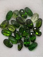 Group of green oval faceted chrome diopside stones on white background