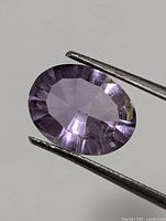 Front view of oval faceted light-purple amethyst held by tweezers