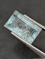 Top view of rectangular step-cut aquamarine held by tweezers