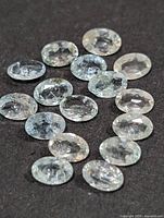 Group shot of all 16 oval aquamarine gemstones on dark background