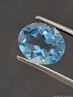 Close-up of oval blue topaz held by tweezers