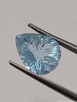 pear-shape blue topaz held in tweezers showing starburst cut