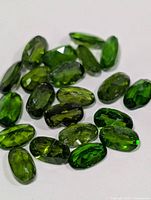 Group of deep green faceted oval chrome diopside stones on white background