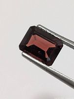 Front view of emerald-cut garnet held by tweezers