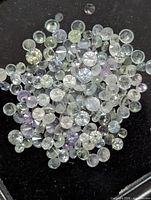 pile of small faceted round gemstones in assorted pale colors