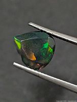 Triangular faceted opal held in tweezers, showing green and orange flashes