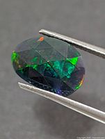 Front view of oval faceted opal held in tweezers